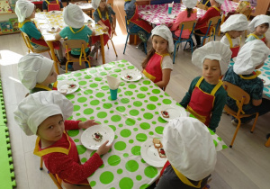 Dzieci siedzące przy stolikach nakrytych kolorowymi obrusami przed swymi deserami tuż przed degustacją.